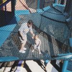 A father and his baby son stand on a net platform.