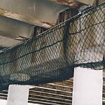 Debris netting wrapping a cement beam under an elevated highway.