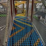 a colorful net bridge connecting elevated climbing structures