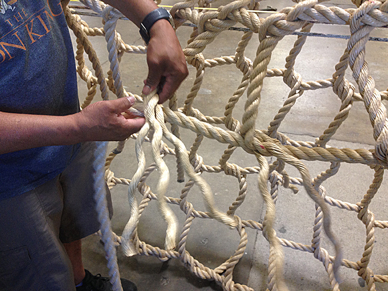 Hand making a rope climbing net.