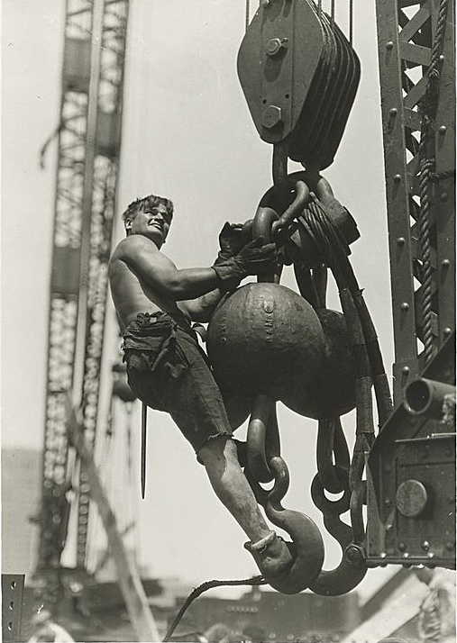 A construction worked rides a crane's lifting cable.