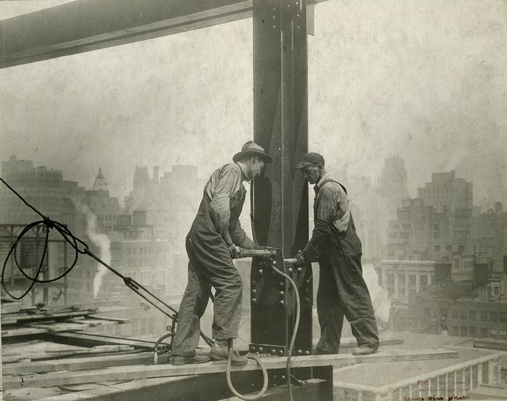 Steel workers applying rivets to a column.