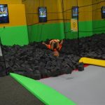A child leaps into a foam cube pit at a tramploine park.